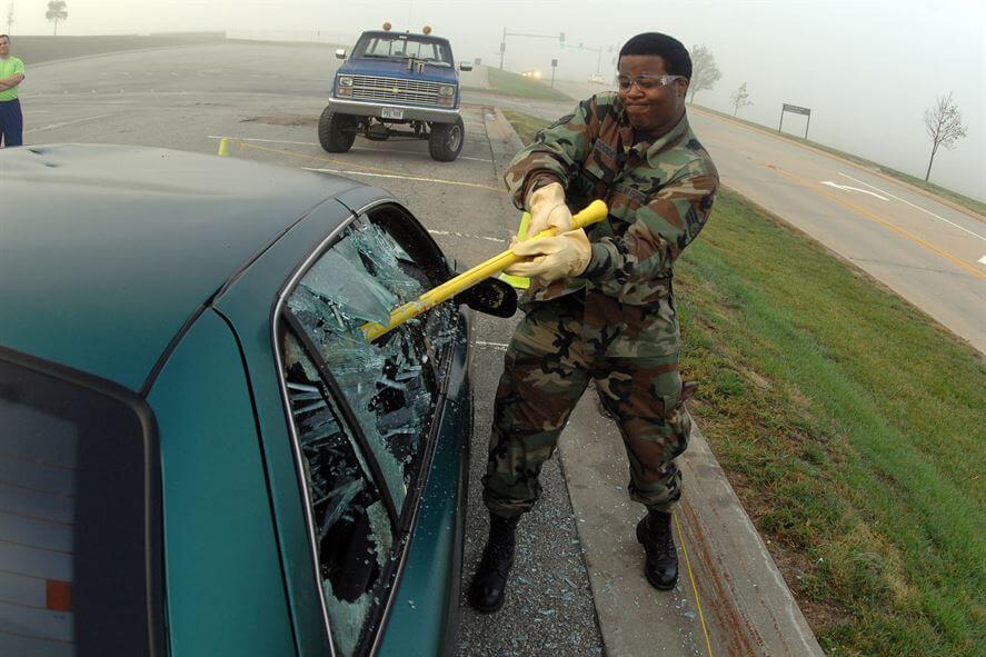 An airman drives a sledgehammer through a car window 